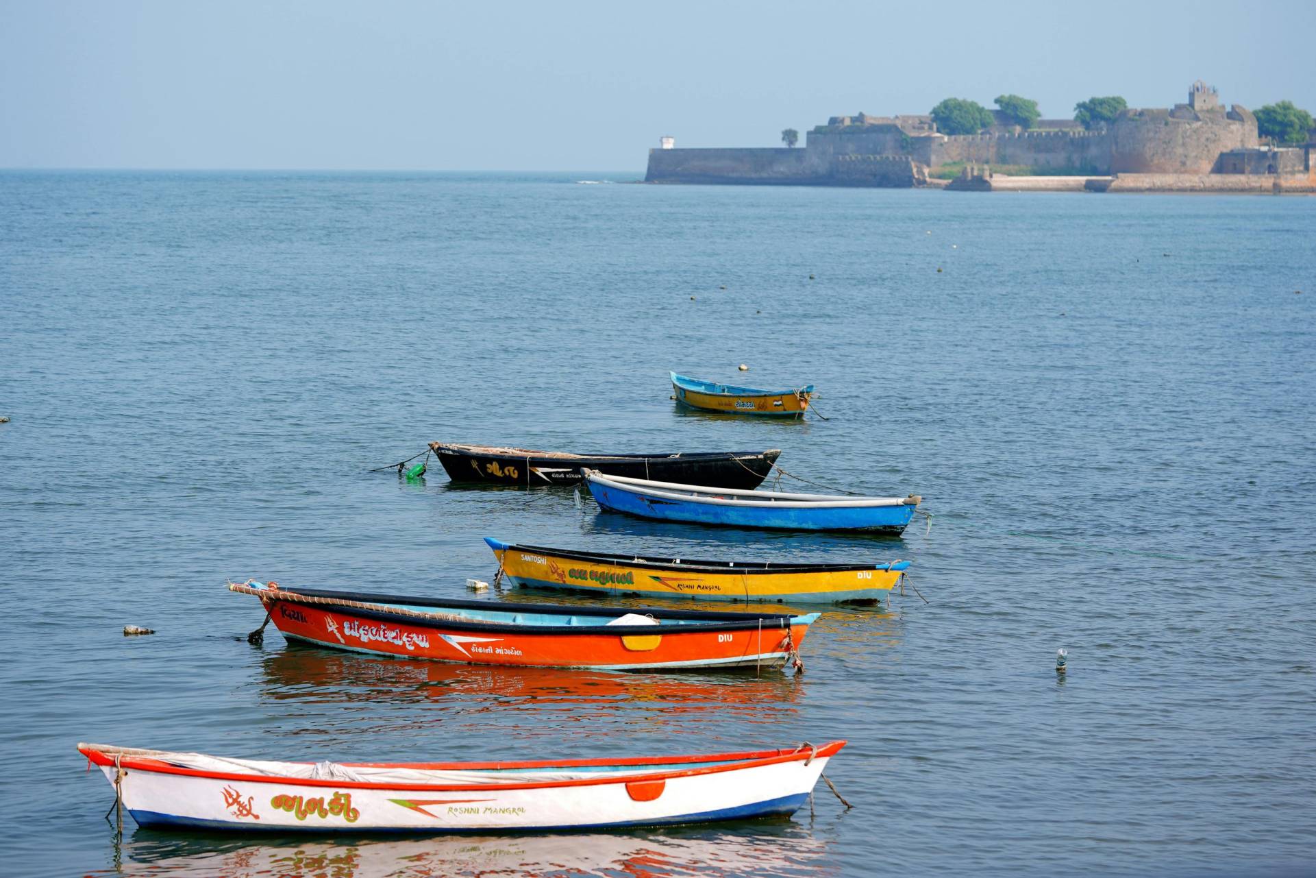 Vibrant boats moored by the seashore with a historic fort in Diu, India.